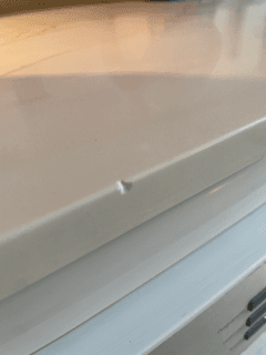 A small chip on the beveled edge of a polished white stone kitchen countertop.