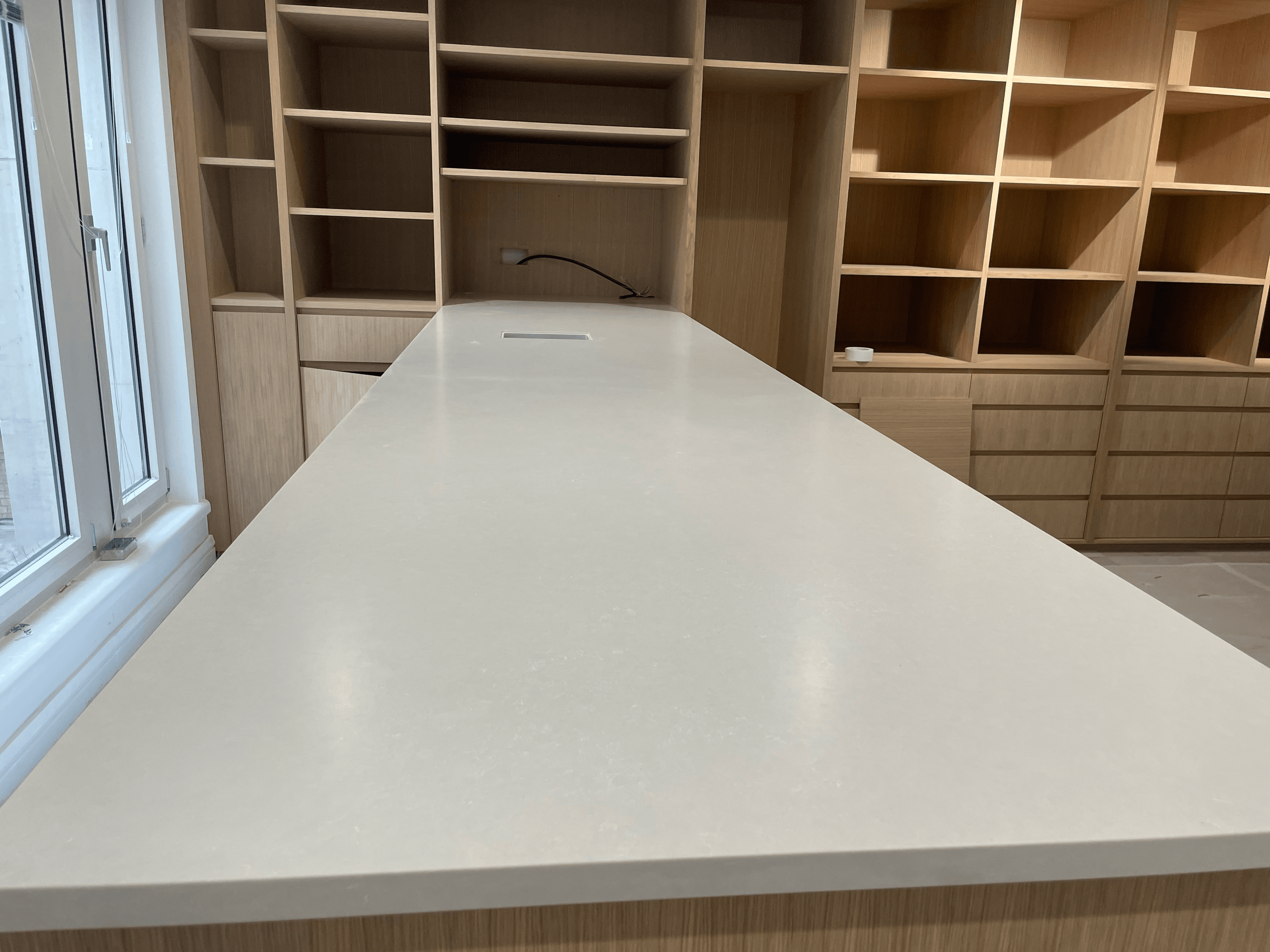 A sleek white countertop stretches toward a wall of empty light wood shelving and cabinetry.
